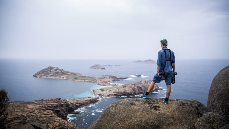A traveler standing on a cliff, overlooking rugged islands and ocean on a Southern Safari -True North Adventure Cruises
