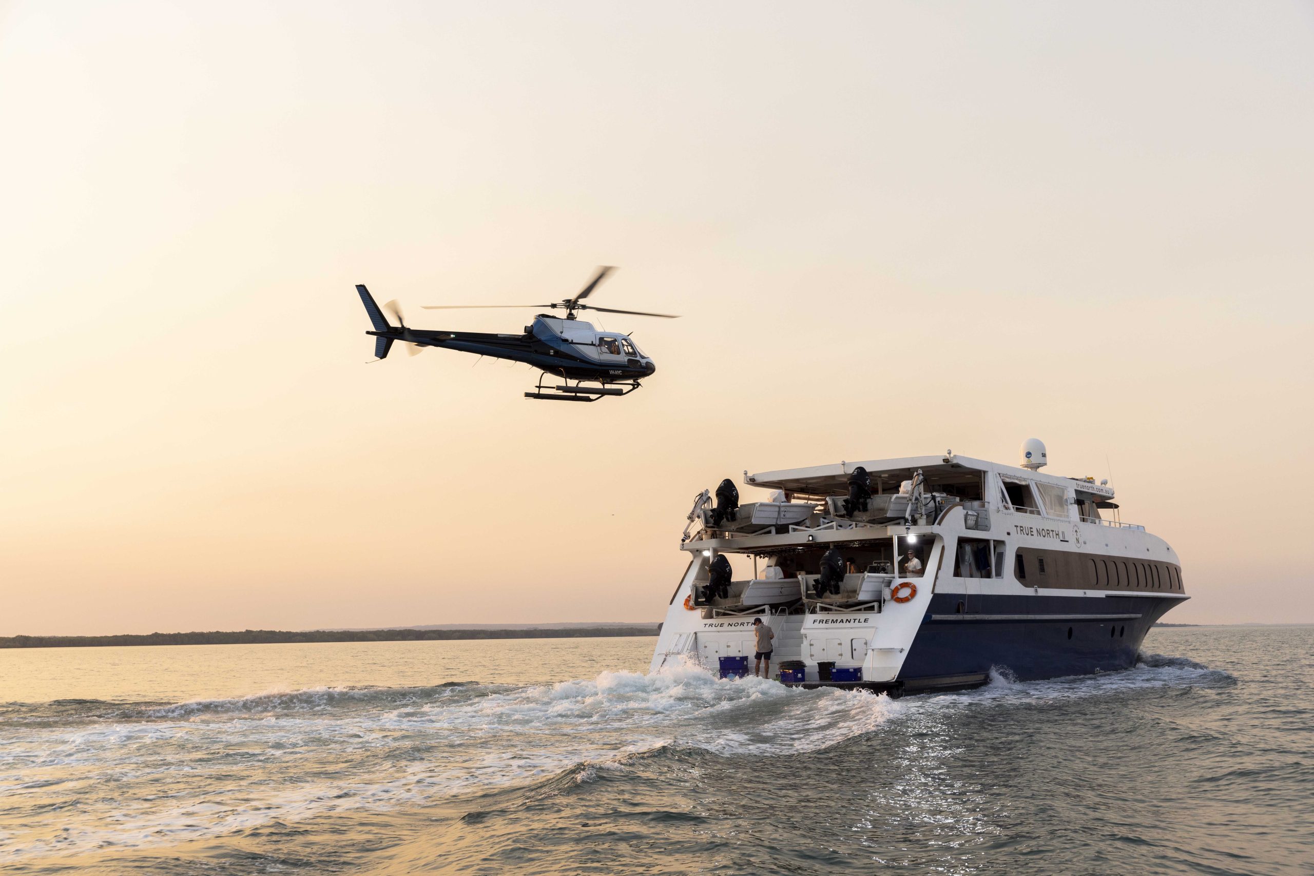Helicopter taking off from the deck of True North cruise ship during a luxury Kimberley expedition, enabling remote access to destinations like Eagle Falls